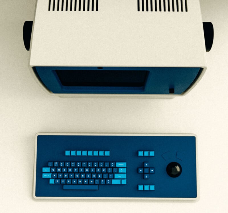 A vintage computer setup with a beige and blue terminal and a matching keyboard featuring blue keys, a large trackball, arrow keys, and function buttons, viewed from above on a light surface.
