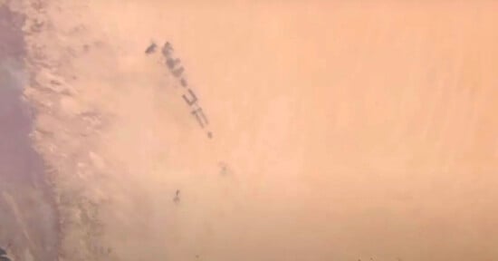 A group of military vehicles moving through a desert landscape, partially obscured by dense clouds of sand and dust.