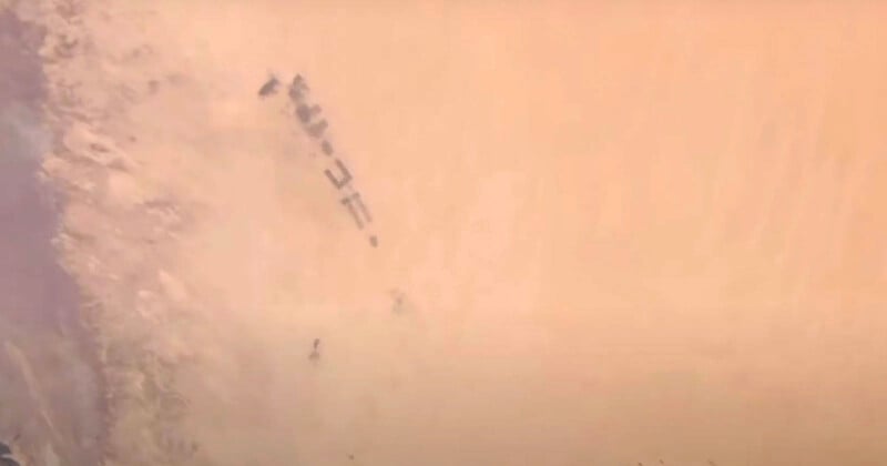 A group of military vehicles moving through a desert landscape, partially obscured by dense clouds of sand and dust.