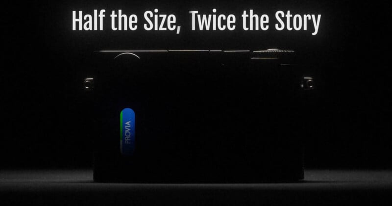 A dark image of a camera with a “PROVIA” label, illuminated by light from above. The top text reads, “Half the Size, Twice the Story” in large white letters.