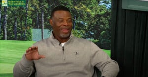 A man in a grey sweater is smiling and gesturing with his hand while sitting. The background shows a forest scene. The top left corner displays the text "MORNINGS @ THE MASTERS" with a green and yellow logo.