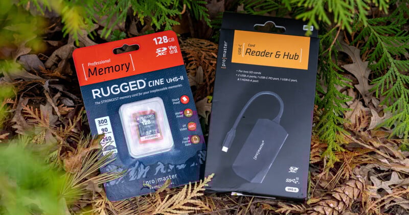Packaging of two tech products placed on autumn leaves. Left: A red and white package for a 128 GB Rugged CINE UHS-II SD card. Right: A black box for a card reader and hub with USB 3.2 and HDMI support. Both are surrounded by green foliage.