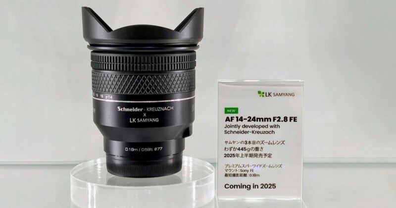 A black Schneider-Kreuznach x LK Samyang camera lens is displayed on a clear stand next to a sign announcing the AF 14-24mm F2.8 FE lens, developed with Schneider-Kreuznach, and coming in 2025.