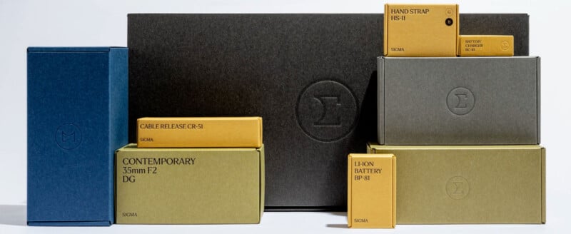 A collection of Sigma product boxes in various sizes and colors, labeled with items such as "CONTEMPORARY 35mm F2 DG," "CABLE RELEASE CR-51," "HAND STRAP HS-11," and "LI-ION BATTERY BP-51.