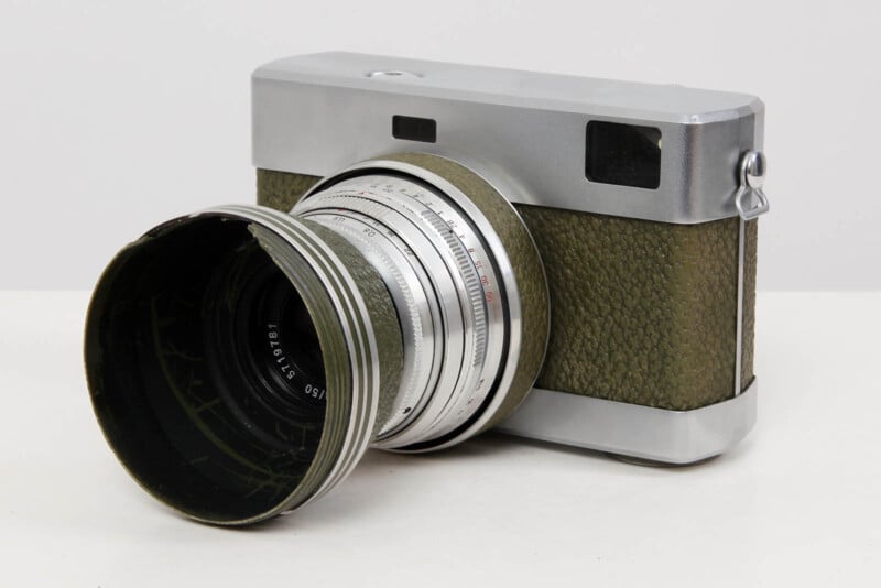 A vintage film camera with a green textured body and a large silver lens, set on a plain white surface.