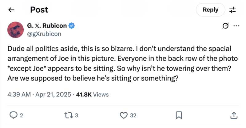A tweet from @xRubicon questions a photo's arrangement, wondering why Joe isn’t taller than others if only he’s standing and everyone else is sitting. The tweet finds the situation bizarre and confusing.