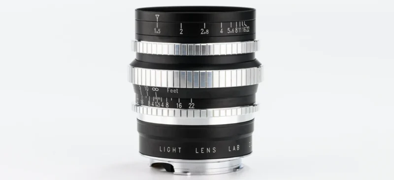 A black and silver camera lens with engraved markings for aperture and focus distances, labeled "LIGHT LENS LAB," displayed upright on a white background.