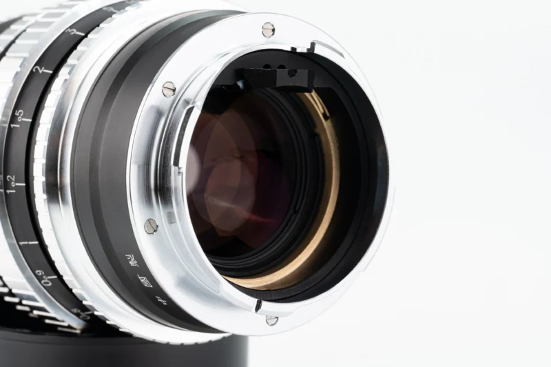 Close-up of the rear side of a camera lens, showing the metal lens mount, glass elements, and alignment marks against a plain white background.